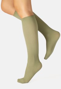 Calcetines hasta la rodilla de color verde oliva con textura de canalé vertical, puño elástico, forma ajustada y acabado suave, adecuados para diversas ocasiones.