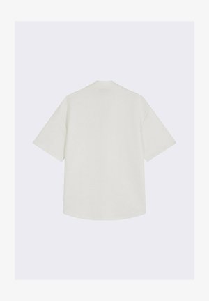 Witte kortoevershirt met een ontspannen pasvorm, voorzien van een subtiel textuurpatroon en een ronde kraag, met een licht gebogen zoom aan de onderkant.