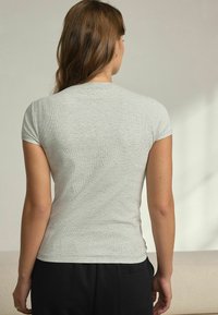 Ljust grå kortärmad t-shirt i ribbat tyg, åtsittande design med rund halsringning, slät textur och subtila sömnadsdetaljer.