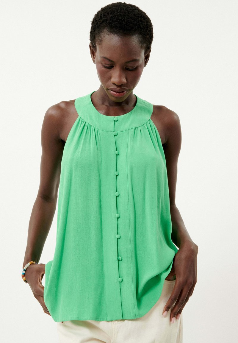 Lichtgroene mouwloze blouse met een ronde kraag, knopen aan de voorkant en zachte stof. Losse pasvorm met een zachte draping rond de torso.