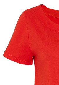 Camiseta de algodón roja de manga corta, con un cuello redondeado y una textura suave. Presenta costuras a lo largo de las mangas y el dobladillo.