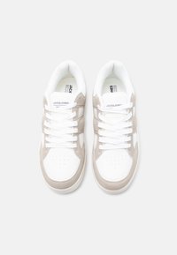 Ζευγάρι λευκών και μπεζ αθλητικών παπουτσιών Jack & Jones με λευκά κορδόνια σε απλό γκρι ανοιχτό φόντο, που φαίνονται από πάνω.