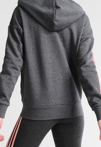 Sweat à capuche gris foncé en matière douce avec une capuche, présentant des rayures roses le long des manches et une ceinture côtelée.