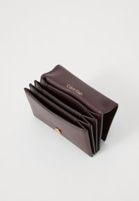 Calvin Klein burgundy leather wallet with gold logo, featuring multiple card slots and a snap closure; smooth texture, compact rectangular shape.