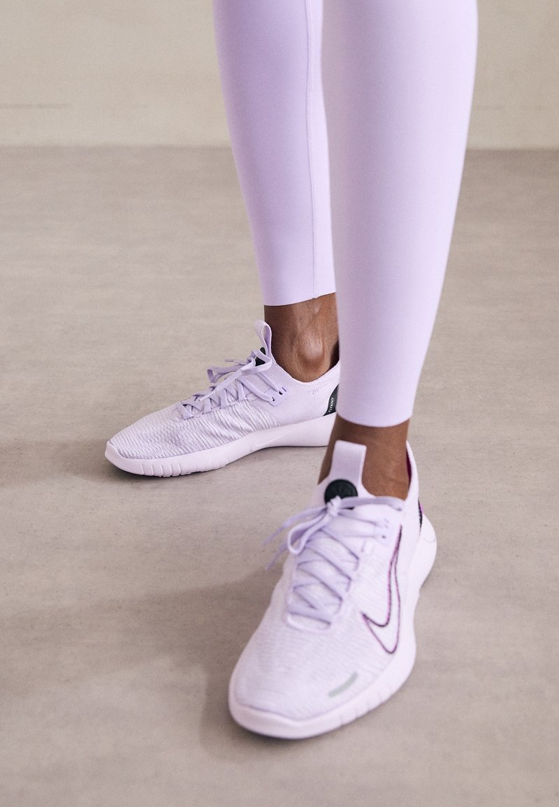 Helllila Sport Schuhe mit einer strukturierten Oberseite, schwarzen Akzenten und weißen Sohlen, kombiniert mit passenden helllila Leggings.