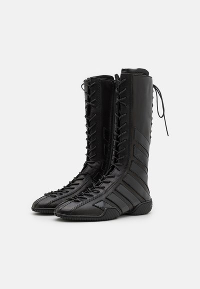 Bottes noires jusqu'au genou en cuir brillant avec un devant lacé et des accents de rayures diagonales. Semelles texturées pour une bonne adhérence.