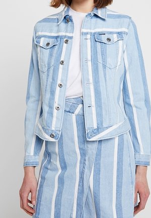 Persoon draagt een lichtblauwe en witte verticaal gestreepte spijkerjas en een bijpassende rok met hoge taille over een wit overhemd.