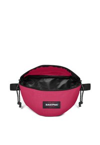 Rund rosa väska gjord av slitstarkt tyg med svart inuti, med dragkedjestängning och Eastpak-logotyp på en svart lapp.