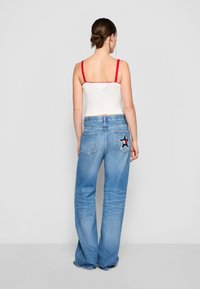 Valkoinen tank-top, jossa on punaiset pitsikoristeet, ja vaaleansiniset levittävät farkut, joissa on tähti-patch takataskussa.