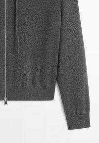 Dark gray knitted zip-up sweater sleeve and lower half on a white background, with silver zipper detailing visible.