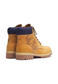 Ein Paar sandfarbener Leder Arbeitsstiefel mit navyblauen, gepolsterten Kragen, Schnürverschlüssen, Gummisohlen und Drachendesigns an den äußeren Seiten.