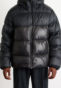 Black puffer jacket with a shiny finish, featuring a hood, zip closure, and horizontal quilted design. Material appears lightweight and insulated.