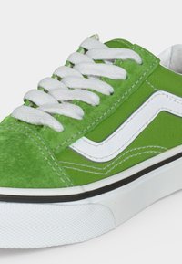 Πράσινο sneaker χαμηλού προφίλ με λευκά κορδόνια, λευκή πλαϊνή ρίγα, μαύρη επένδυση και υφασμένη λευκή ελαστική σόλα, εμφανιζόμενο από πλάγια γωνία.