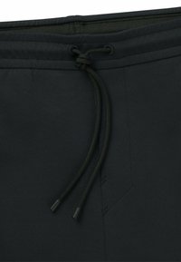 Mustat urheilushortsit, joissa on sileä pinta, joustava vyötärö, jossa on vihreä nauha, ja sivusaumayksityiskohtia hengittävän istuvuuden takaamiseksi.