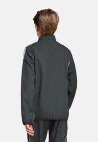 Schwarze Sportjacke mit hohem Kragen, elastischen Bündchen und zwei seitlichen Streifen in Weiß; aus leichtem, glattem Stoff gefertigt.