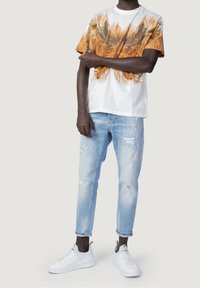 White short-sleeve t-shirt with orange palm leaf print; worn with light blue distressed jeans and white sneakers. Casual outfit.