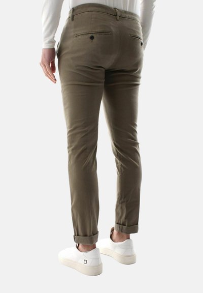 Olivengrønne bukser med skræddersyet pasform, der har baglommer og opfoldede kanter, parret med hvide sneakers. Glat stoftekstur.