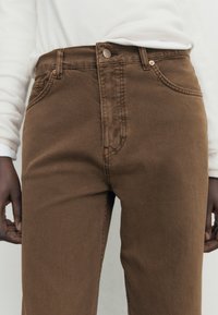 Bruna denimjeans med hög midja, klassisk femfickdesign och en jämn yta. Har en metallknäppning och bälteshällor.