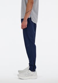 Marineblauwe sportbroek met een slim fit, gemaakt van lichtgewicht materiaal, met ritsen bij de kuiten en gecombineerd met witte hardloopschoenen.