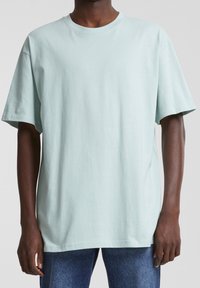 T-shirt en coton vert menthe clair avec un col rond classique, des manches courtes et une coupe décontractée, associé à un jean en denim bleu.