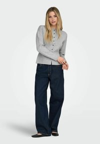 Siv pleteni jopica z okrolim izrezom in gumbi, kombinirana z ohlapnimi temno modrimi kavbojkami in črnimi čevlji z nizkim podplatom. Gladek videz.