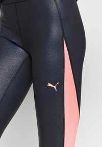 Svarta sportleggings med en glänsande yta, med en sidopanel av rosa mesh och en liten ljusrosa Puma-logotyp nära knät.