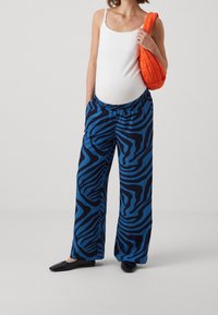 Blue and black zebra-striped wide-leg pants with an elastic waistband and a relaxed fit, paired with a white tank top and black flats.
