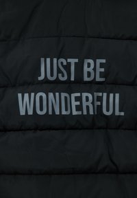 Tela negra acolchada con costuras horizontales y el texto "SIMPLEMENTE SÉ MARAVILLOSO" en letras grises y negrita en el centro.