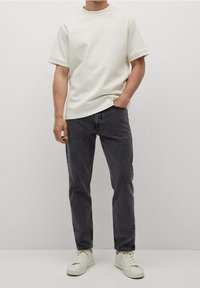 Valkoinen, lyhythihainen t-paita, rento istuvuus, yhdistetty tummanharmaiden farkkujen ja vaaleiden lenkkareiden kanssa. Yksinkertainen malli, pehmeä pinta, ei näkyviä kuvioita.