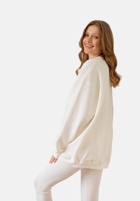 Biała, oversize'owa bluza z długimi rękawami i ściśniętymi mankietami, wykonana z miękkiej tkaniny, w połączeniu z dopasowanymi, białymi legginsami.