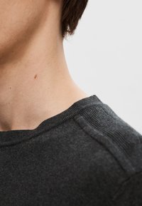 Dark gray sweater with a ribbed crew neckline and subtle shoulder seam detail, made from a soft, textured fabric.