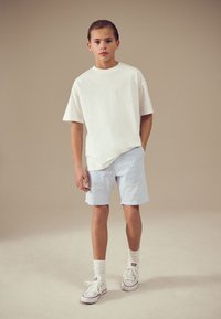 Bela bombažna majica, svetlo modre in bele črtaste kratke hlače, beli supergi in bele nogavice. Prijeten in preprost dizajn za vsakdanjo uporabo.