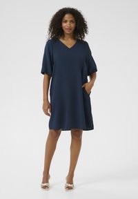 Navy blue short-sleeve dress with a V-neck, relaxed fit, textured fabric, and side pockets, reaching mid-thigh in length.
