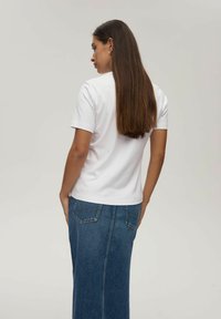 Biała koszulka z krótkim rękawem połączona z długą dżinsową spódnicą. Materiał wydaje się miękki, z niebieskimi szwami i dwoma tylnymi kieszeniami.