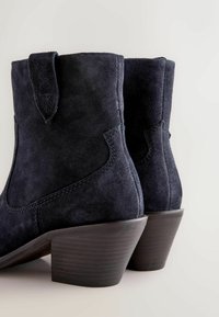 Stivali alla caviglia in suede blu navy con tacco curvo, dotati di un pratico tassello laterale e cuciture tonali, progettati per coprire la caviglia.