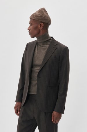 Dunkel gestreifter Anzug mit taillierter Passform, kombiniert mit einem braunen Rollkragenpullover und einer gerippten Strickmütze. Glatter Stoff, scharfe Revers und Taschen.