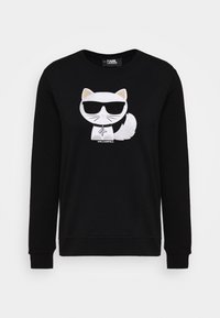 Sudadera negra con un gato de dibujos animados de cara blanca, que lleva gafas de sol y un logotipo gráfico. Material suave y texturizado con puños acanalados.