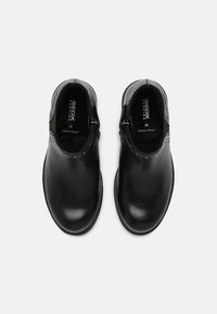 Zapatos de cuero negro con textura suave, punta redondeada, cierre lateral con cremallera y costuras en contraste a lo largo del borde superior. Talla 28.