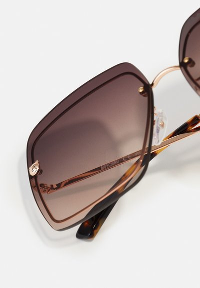 Lunettes de soleil carrées avec des verres dégradés marron, des branches écaille de tortue et des accents en métal doré. Nom de la marque "Moschino" imprimé sur la branche.