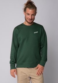 Donkergroene sweatshirt met lange mouwen en een ronde hals. Heeft een witte "GO GREEN!" tekst op de linkerborst. Van katoen, casual pasvorm.