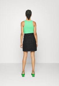 Green sleeveless top paired with a black denim skirt, featuring a waistband and two back pockets; model wears chunky green heeled sandals.