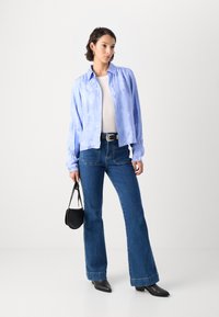 Lyseblå button-up skjorte med blomsterdesig, hvit tettsittende topp, mørke utsvingte jeans, svarte ankelboots og en liten svart håndveske.