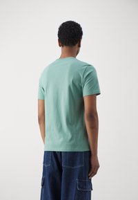 T-shirt vert menthe à manches courtes en coton, avec un col rond et une texture lisse, porté avec un pantalon cargo bleu.