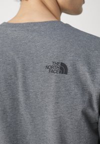Siva pamučna majica s crnim ispisanim logotipom "The North Face" na gornjem dijelu leđa. Kratki rukavi i dizajn s okruglim izrezom.