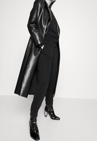 Svart läderjacka med glansig yta, lager på lager över en svart sweatshirt och sweatpants. Innehåller stiliga ankelskor med metallklackar.