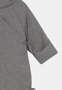 Grå, langermet plagg i myk tekstil med omslagdesign. Har en knyttedetalj på siden og synlige sømmer langs skjøtene.