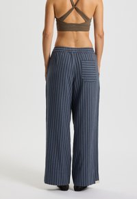 Pantaloni a gamba larga in blu navy con righe verticali. Realizzati in tessuto leggero, presentano una vita elasticizzata e una tasca posteriore singola.