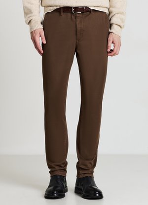 Braune Hose mit glatter Textur, schmaler Passform und Gürtelschlaufen. Kombiniert mit einem beigen Pullover und schwarzen Lederschuhen.