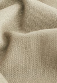 Tissu tissé beige avec une texture lisse et douce, des fils diagonaux fins visibles créant des plis doux.