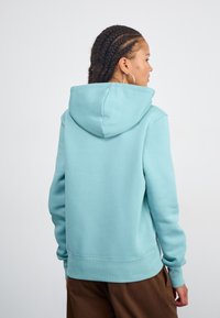 Sweat à capuche turquoise clair avec une capuche spacieuse et des poignets côtelés, fabriqué à partir d'un matériau doux, présente un design minimaliste sans motifs.